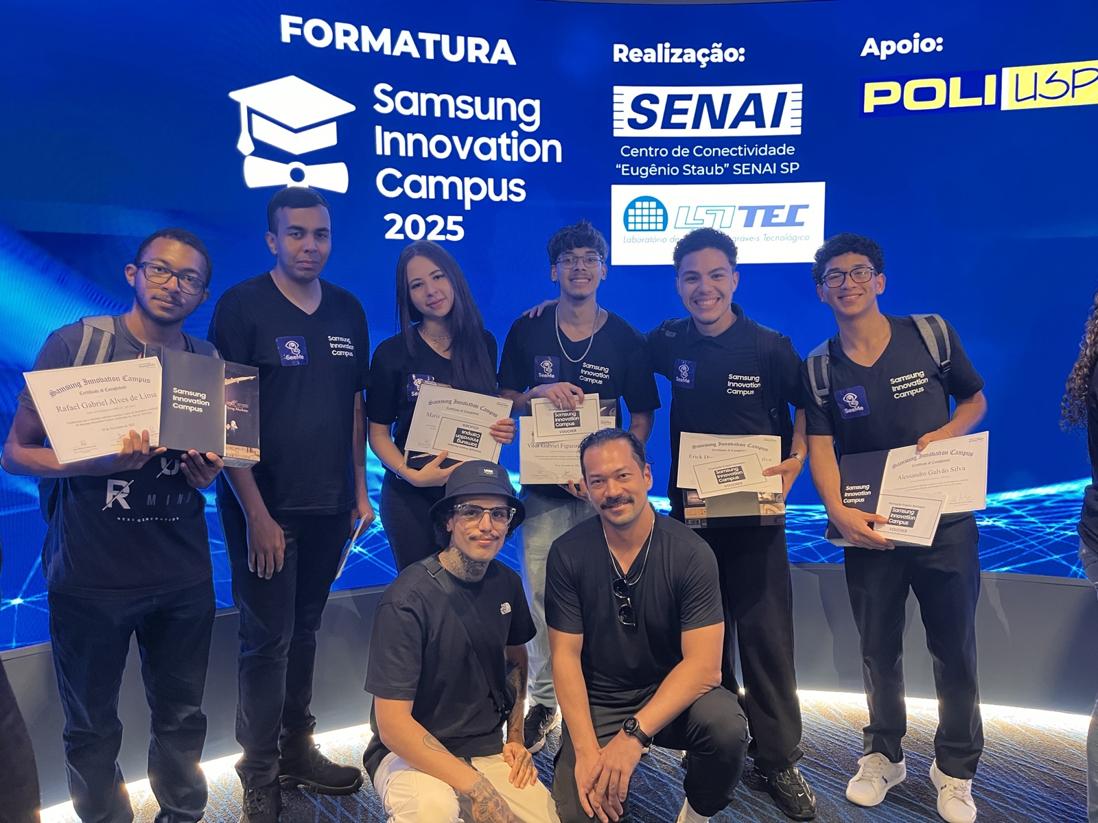 A turma da formatura segurando os certificados, diante do painel do Samsung Innovation Campus 2025