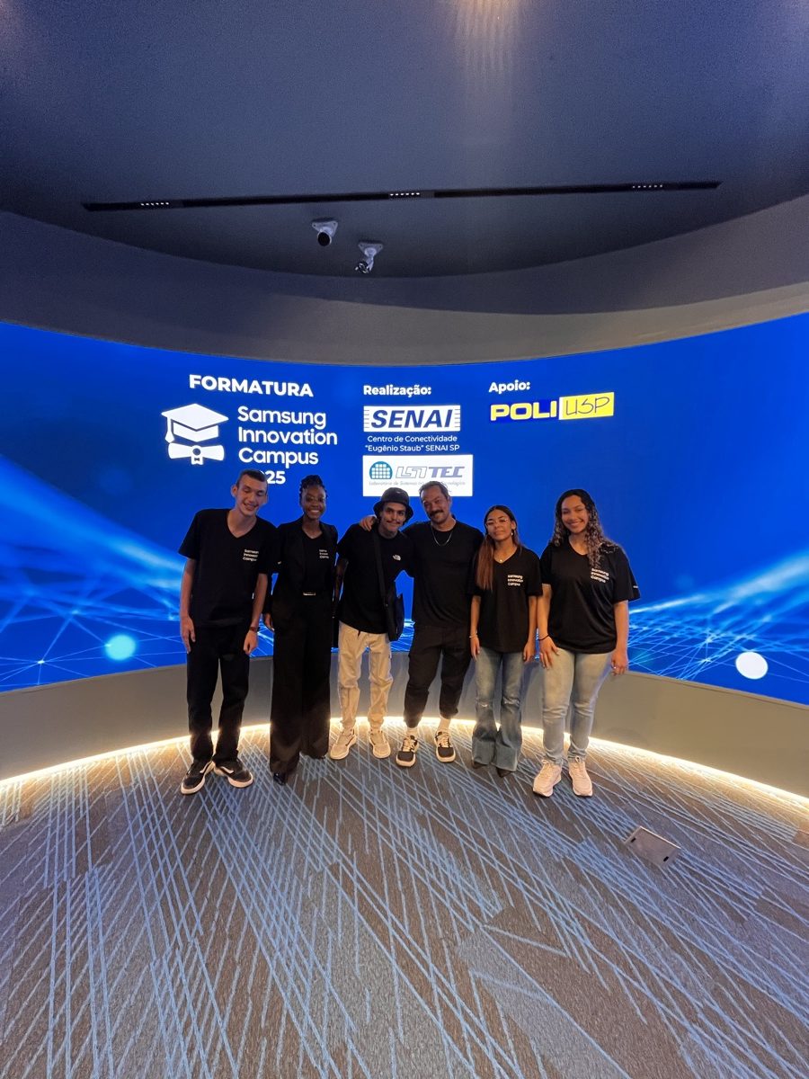 Seis pessoas lado a lado diante do painel curvo da formatura